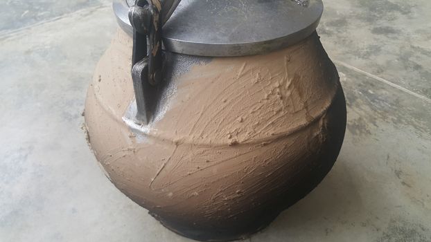 Pressure cooker covered with mud for cooking on fire. Cauldron type rural pressure cooker.