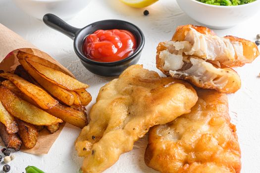 Fishand chips battered crispy cod fillet detail with dip and lemon in a paper cone on white background with all components classic recipe takeaway food white stone textured background side view .