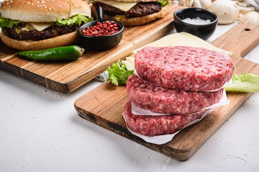Raw ground beef meat cutlets for burger on white textured background.