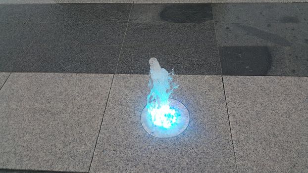 Beautiful and colorful light water fountain over concrete floor. Colorful water shape on fountain with grey background.