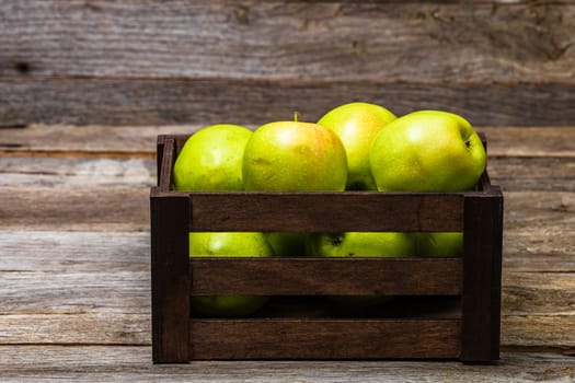 Wooden crate with ripe green apples on wooden table.