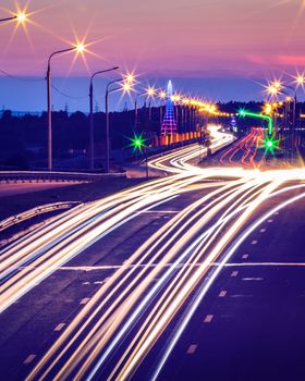 Traces of headlights from cars moving at night on the bridge, illuminated by lanterns. Abstract city landscape with highway at dusk. 