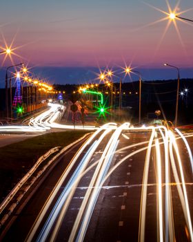 Traces of headlights from cars moving at night on the bridge, illuminated by lanterns. Abstract city landscape with highway at dusk. 