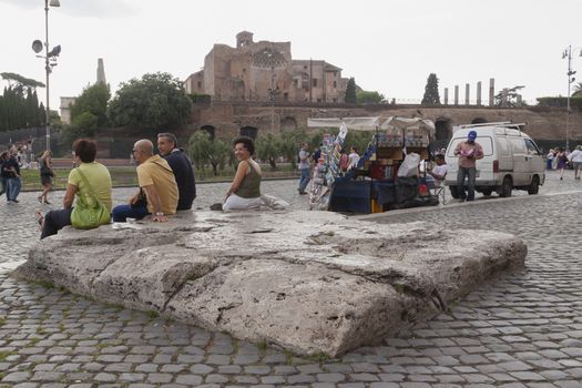 Rome, Italy - June 27, 2010: A woman, probably a tourist, looks at the camera and smiles, while resting with a group of people near the Colosseum in Rome, in the square of the Arch of Constantine.