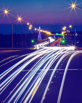 Traces of headlights from cars moving at night on the bridge, illuminated by lanterns. Abstract city landscape with highway at dusk. 