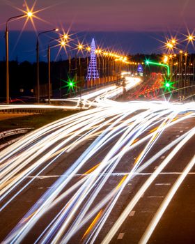 Traces of headlights from cars moving at night on the bridge, illuminated by lanterns. Abstract city landscape with highway at dusk. 