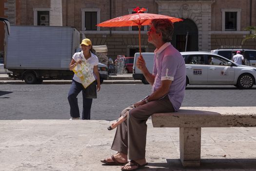 Rome, Italy - June 28, 2010: A street vendor of umbrellas, remains seated on a bench, next to a woman who works as a tour guide in Rome.