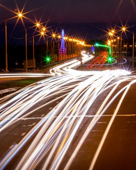 Traces of headlights from cars moving at night on the bridge, illuminated by lanterns. Abstract city landscape with highway at dusk. 