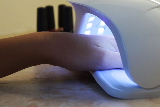 female hand in a UV lamp for drying gel polish close up