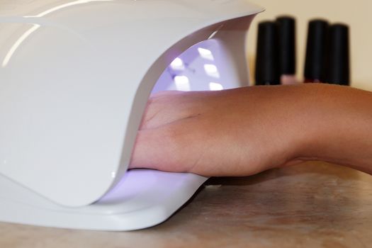 female hand in a UV lamp for drying gel polish close up