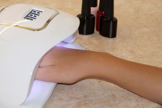 female hand in a UV lamp for nail manicure close up