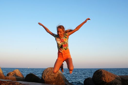 joyful teenage girl with raised arms in a jump against the background of the sea.