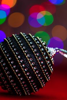 Black and shiny Christmas ball bauble in a Christmas composition on blurred lights background.