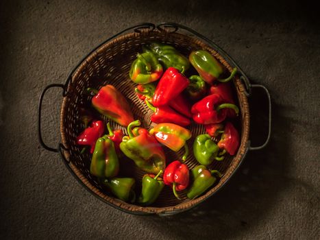 Basket with green and red peppers on a grey stone surface