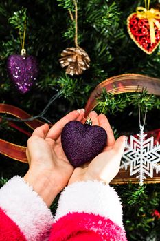 Hands holding Christmas ornament in front of Christmas tree. Decorating fir branches with Christmas decorations.