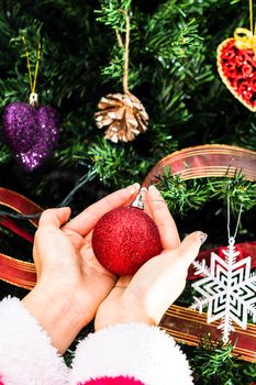 Hands holding Christmas ornament in front of Christmas tree. Decorating fir branches with Christmas decorations.