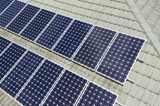 Blue solar panels on a green tiled roof in the bright sunshine.