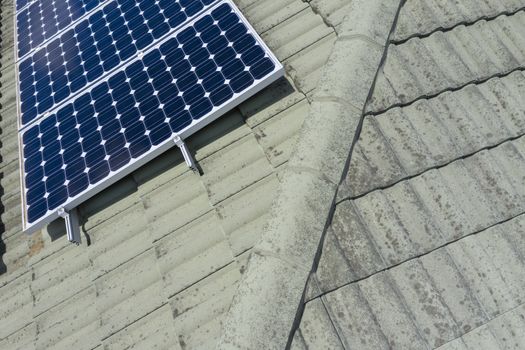 Blue solar panels on a green tiled roof in the bright sunshine.