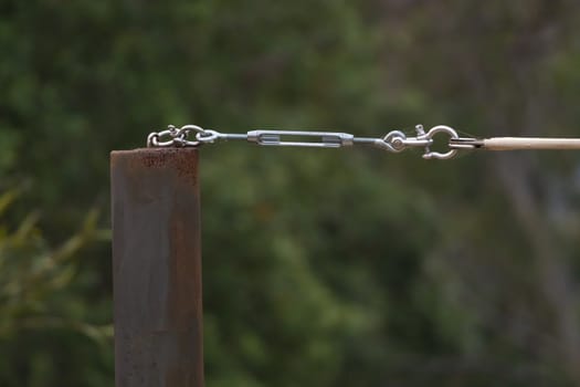 A stainless steel turnbuckle shackle connected to a black metal pole holding up a shadecloth