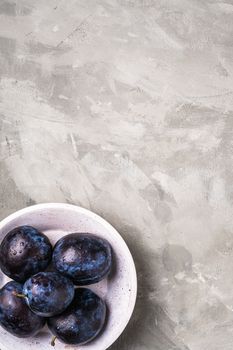 Fresh ripe plum fruits with water drops in wooden bowl on stone concrete background, top view copy space