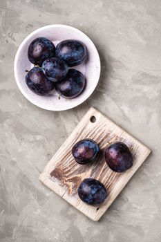 Fresh ripe plum fruits with water drops in wooden bowl and cutting board on stone concrete background, top view