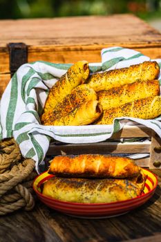 Sausages baked in dough sprinkled with salt and poppy seeds in a rustic composition. Sausages rolls, delicious homemade pastries.