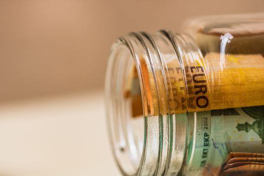 Concept of investing and keeping money, close up isolated. Composition with saving money banknotes in a glass jar. Detail of euro banknotes in jar.