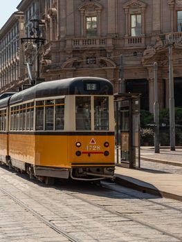 A yellow tram passes through the streets of the city of Milan, a historic Italian public transport