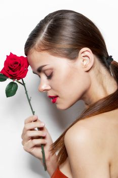 Woman with bare With his eyes closed he holds a rose near his face shoulders charm light background