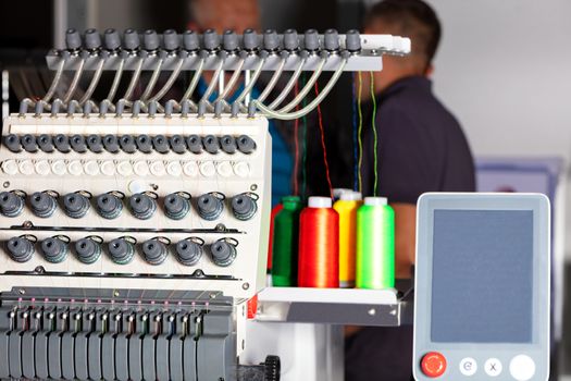 Modern professional embroidery machine for embroidery on various fabrics with a display and multi-colored spools of thread in a blur, a place for text.
