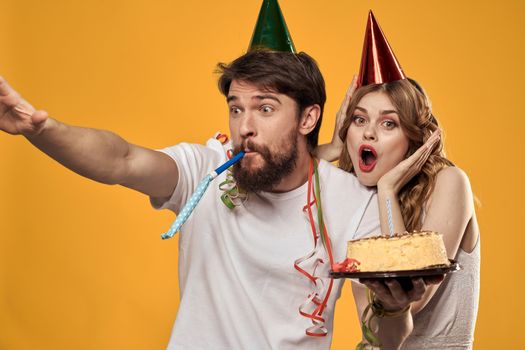 Man and woman birthday festive cake yellow background and caps on the headv. High quality photo