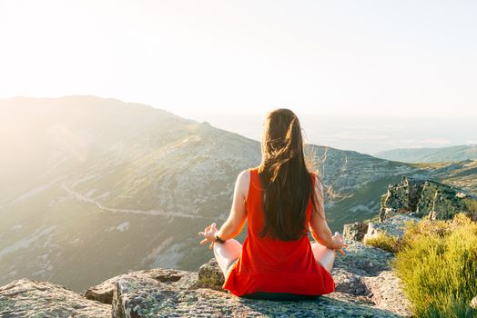 Woman practices yoga and meditates on the mountain.