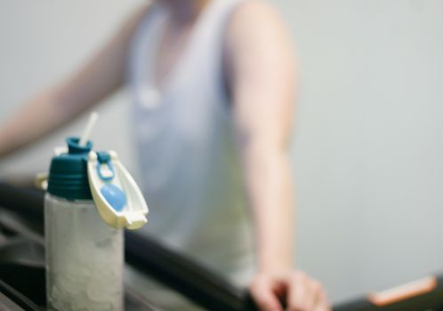 blur photo of water bottle and tired woman jogger on treadmill