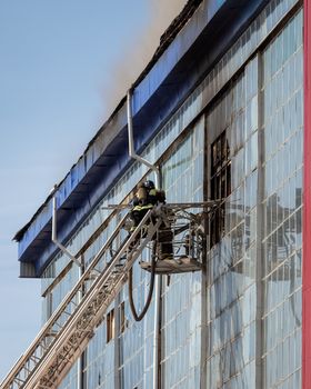 Russia, Kaluga - SEPTEMBER 08, 2020: A team of firefighters in protective suits and helmets on the stairs extinguishing a fire in a building with a broken window and blue roof.