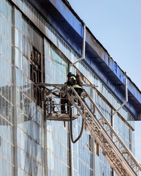 Russia, Kaluga - SEPTEMBER 08, 2020: A team of firefighters in protective suits and helmets on the stairs extinguishing a fire in a building with a broken window and blue roof.