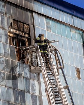 Russia, Kaluga - SEPTEMBER 08, 2020: A team of firefighters in protective suits and helmets on the stairs extinguishing a fire in a building with a broken window and blue roof.