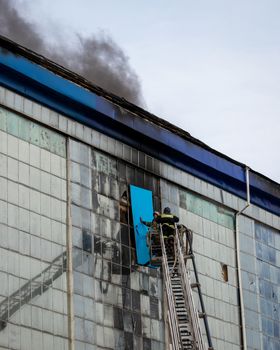 Russia, Kaluga - SEPTEMBER 08, 2020: A team of firefighters in protective suits and helmets on the stairs extinguishing a fire in a building with a broken window and blue roof.