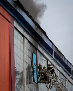 Russia, Kaluga - SEPTEMBER 08, 2020: A team of firefighters in protective suits and helmets on the stairs extinguishing a fire in a building with a broken window and blue roof.