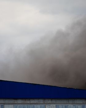 Black smoke rising from a burning building with a cloudy sky in the background.
