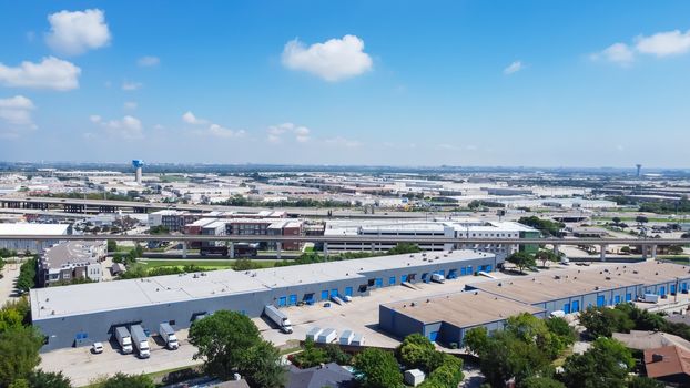 Top view logistic center and industrial warehouse park near historic downtown Carrollton Square, Texas. Elevated highway and pedestrian bridge over Belt Line Road in background, residential houses on left