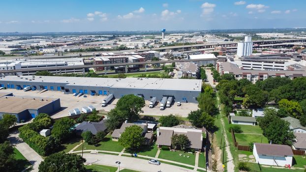 Top view logistic center and industrial warehouse park near historic downtown Carrollton Square, Texas. Elevated highway and pedestrian bridge over Belt Line Road in background, residential houses on left