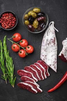 Spanish longaniza salami sausage slices with herbs on balck background, top view.