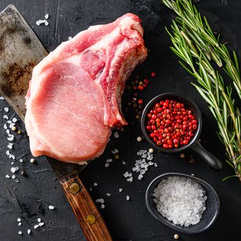 Organic cutlet on a rib or Pork meat over american classic butcher knife or cleaver with spices and rosemary and red pepper on black slate table top view. Square