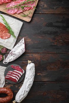 Variety of dry cured chorizo, fuet and other sausages cut in slices with herbs on dark wooden background with space for text.