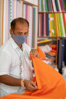 Shopkeeper in medical mask measuring cloth using scale or ruler - concept of back to business, business reopen after covid-19 or coronavirus pandemic