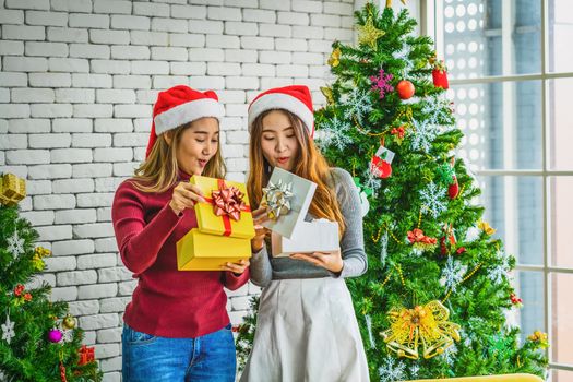 LGBTQ couple asian happiness women wearing colorful red sweaters holding and opening the Gift Box in christmas party with xmas trees, asian or asean indoor, xmas and new year concept