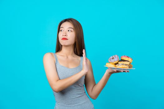Attractive Asian young woman doing no action with donuts on isolated blue color background, weight loss and avoid junk food for dieting and Healthy concept, copy space and studio