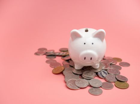 White piggy bank Placed on top of a pile of coins On a pink background. saving money concept.