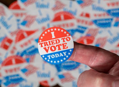 Finger with I Voted button in front of voting stickers given to US voters in Presidential election to illustrate vote suppression or rejections
