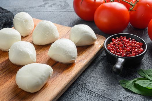 Buffalo Mozzarella cheese balls with fresh basil leaves and cherry tomatoes, the ingredients of the Italian Caprese salad, on a black cloth and grey concrete background close up.